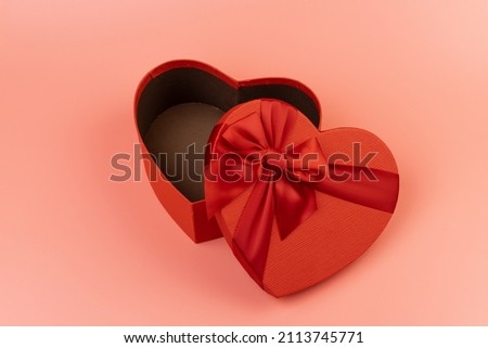 Red heart-shaped gift box with a red ribbon on pink background. Happy Valentine's Day. Anniversary. 
