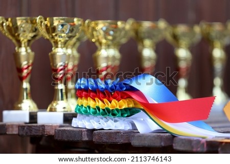Group of equestrian sport trophies and badges rosettes at equestrian event in row. Pile of sport trophies and badges rosettes for the winners on show jumping competition