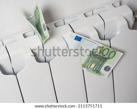 Close-up of one hundred euro bills inserted into a white central heating battery. The concept of high payments for heat in winter in Europe.