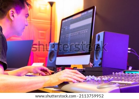 asian music producer, sound engineer, DJ hands mixing music tracks on digital mixer console in home recording studio. focus on hand. music production, recording concept