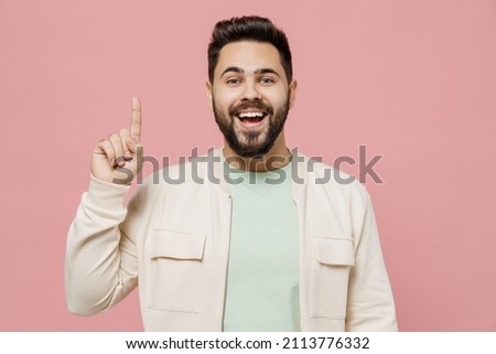 Young smiling happy caucasian man 20s wearing trendy jacket shirt holding index finger up with great new idea isolated on plain pastel light pink background studio portrait. People lifestyle concept