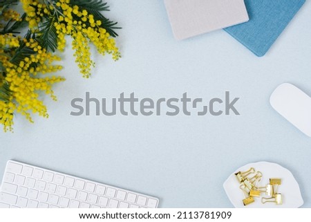 On a blue flat lay background with a yellow mimosa flower, keyboard notepad and stationery clips, a female floral desktop. The concept of a stylish spring morning. top view and copy space Royalty-Free Stock Photo #2113781909