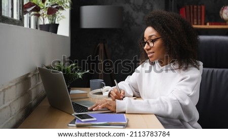 African young teenager e-learning on distance, using laptop, writing homework assignment in copybook, watching webinars online from home. Royalty-Free Stock Photo #2113783784