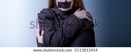 girl with a gag in her mouth as a symbol of censorship. Silence of issues of discrimination.Woman victim with black scotch and closed pose.Concept of slavery, violence,childish harassment Royalty-Free Stock Photo #2113813454