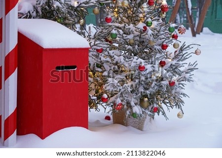 A red letter box for Santa Claus and a Christmas tree decorated with balloons are standing in the park in the snow