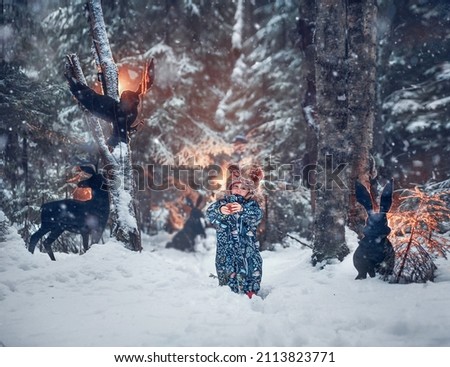 Fairy picture of little girl in beautiful overall and funny fur foxhead-like hat in front of animal silhouettes in winter park. Image with selective focus and toning.