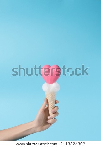 Pink heart shaped icecream with cloudy creme held in hand in blue background