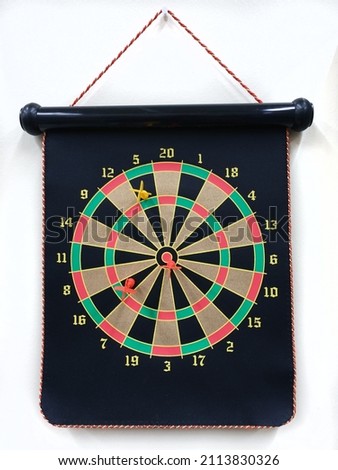 Magnetic dartboard with darts hanging from white office wall.