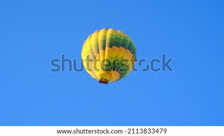 beautiful bright yellow green hot air balloon flies in bright blue cloudless sky. Dawn light hits balloon from one side, which is controlled by balloonist.