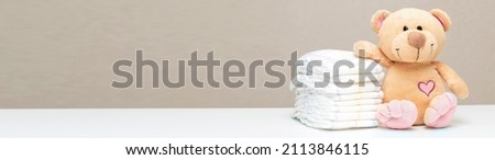 Stack of diapers for baby, toddler with toy teddy bear on table. set for boy girl for baby shower with copy space, banner. Royalty-Free Stock Photo #2113846115