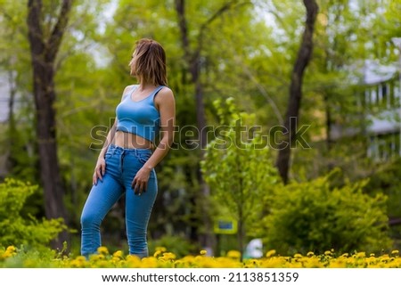 Young woman in a city park during dandelion flowering. Yellow cheerful lightning concept. Symbol of happiness and freedom
