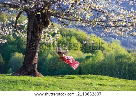 A girl in a romantic image swings on a swing. Beautiful, lush, flowering cherry tree is dotted with flowers. Naturel spring landscape.