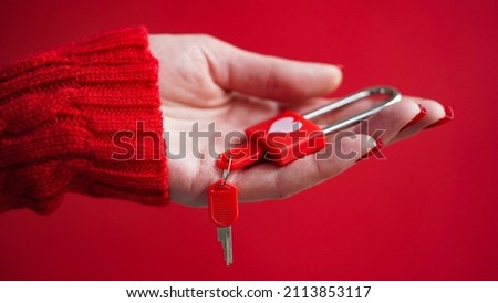 Close-up of a woman's hand in a red sweater holding a padlock with a heart with keys on a red background.The concept of Valentine's day,wedding,a symbol of love and fidelity.Red lock