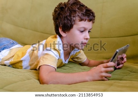 boy in yellow and white t-shirt enthusiastically plays a game on a tablet