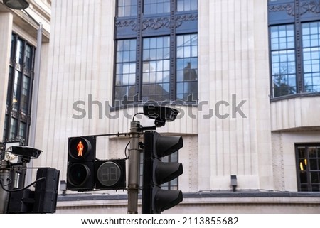 Pedestrian red traffic light with security camera installed on pole against building, Red traffic light with security cameras on pole