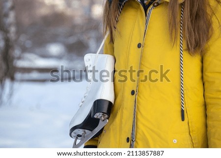 Close up of female hands holding ice skates. Young woman in yellow coat with skates.