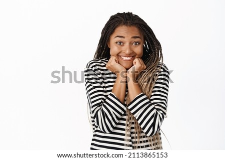 Smiling excited black girl waiting for smth with anticipation, yearning, looking with interest and amusement at camera, standing over white background Royalty-Free Stock Photo #2113865153