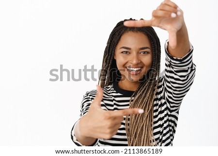 Portrait of smiling african american woman making hand frames and searching for perfect angle, shooting photo, creating image, standing over white background
