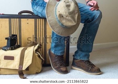 a male traveler in jeans and old boots sits on a vintage suitcase waiting for departure.