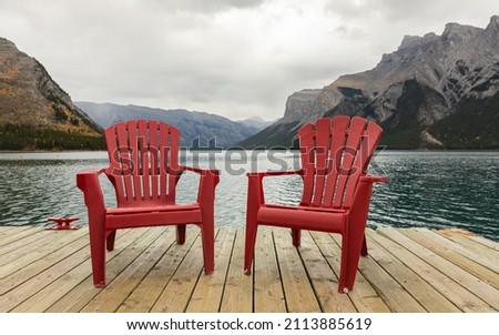 Two bright red Adirondack chairs in Banff National Park, Canada. Two red comfortable deck chairs on the lake. Travel photo, street view, nobody, selective focus, copyspace for text