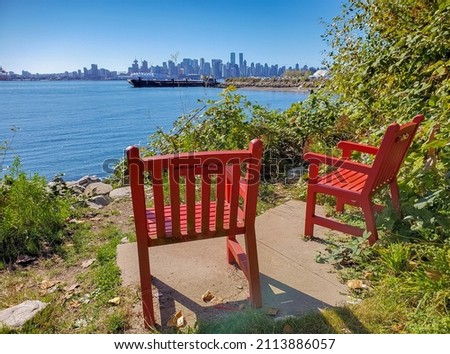 Two bright red Adirondack chairs in Harbour of Vancouver Park, Canada. Two red comfortable deck chairs by the waterfront. Travel photo, street view, nobody, selective focus, copyspace for text