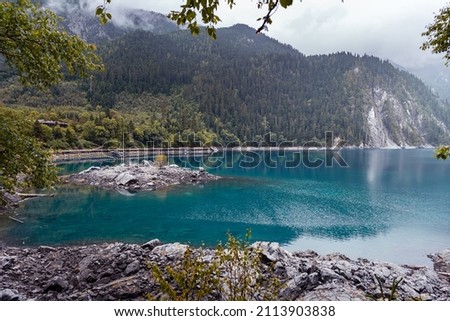 Shores of the Long Lake with mountains in the clouds, Jiuzhaigou Valley Scenic Area, Sichuan, China  Royalty-Free Stock Photo #2113903838