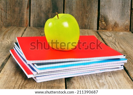 Green apple and writing-books. On wooden background.