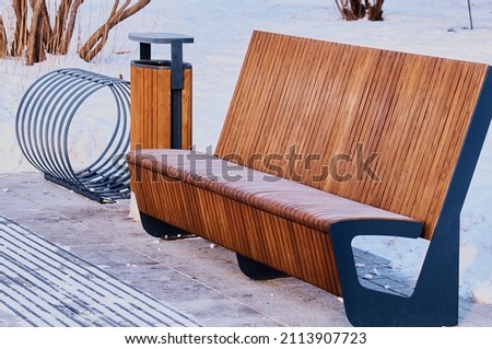 Futuristic wooden bench with an urn in a snowy winter park on a snow-cleared site. Quarantine concept. Convenient eco-friendly design. Geometry of parallel lines. Bicycle holder in the same style.