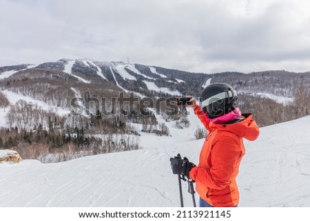 Winter Skiing woman. Alpine ski - skier taking pictures using phone looking at mountain view against snow covered trees and ski in winter. Mont Tremblant, Quebec, Canada