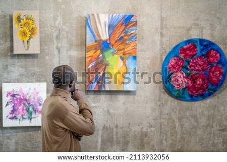 African young man examining the modern art on the wall while visiting art gallery