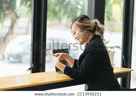 Portrait of a cheerful asian woman looking at the street while sitting in a coffee shop with a mobile phone in her hands. Business woman happy to read good news on a smartphone form business partners