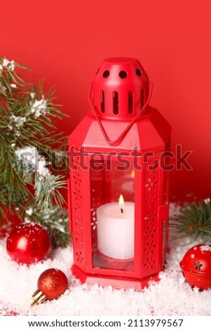 Christmas lantern with burning candle, fir branch and balls on red background