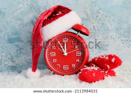 Stylish New Year clock, Santa hat, gloves and snow on blue background