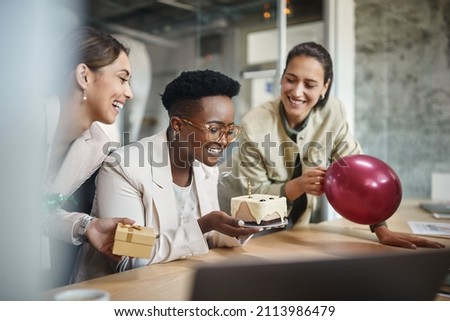 Happy African American businesswoman blowing out a candle on cake while celebrating Birthday with female coworkers in the office. 