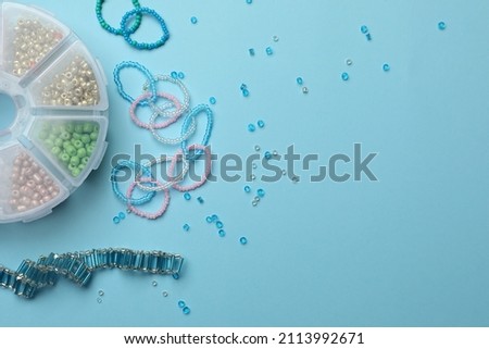 Beautiful handmade beaded jewelry and supplies on light blue background, flat lay. Space for text