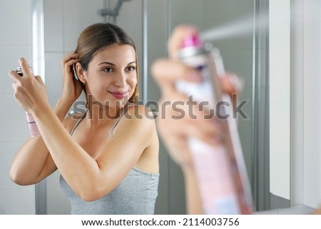 Young woman applying dry shampoo on her hair before going out. Fast and easy way to covering grey hair with instant spray dye. Royalty-Free Stock Photo #2114003756