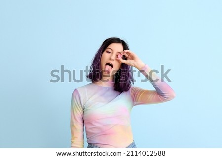 Stylish young woman with pink chewing gum showing tongue on blue background