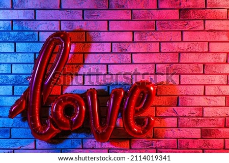Balloon in shape of word LOVE hanging on color brick wall. Valentine's Day celebration