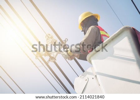 Electrical power line technicians perform maintenance on power lines by using a truck-mounted bucket. Royalty-Free Stock Photo #2114021840