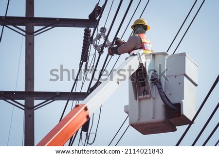 Electrical power line technicians perform maintenance on power lines by using a truck-mounted bucket. Royalty-Free Stock Photo #2114021843