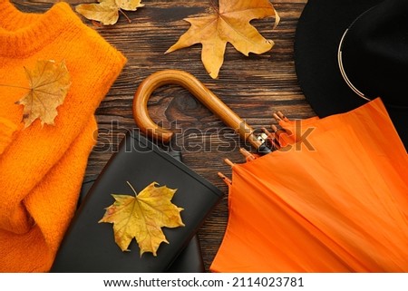 Autumn composition with umbrella, hat, sweater and rubber boots on wooden background, closeup