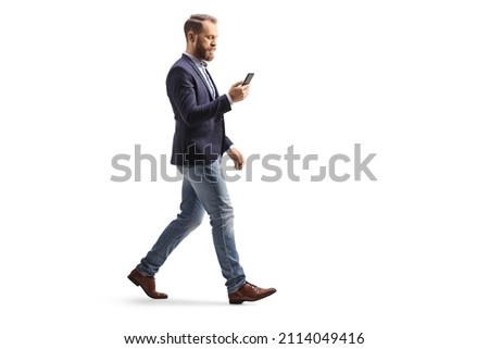 Full length profile shot of a man in suit and jeans using a mobile phone and walking isolated on white background Royalty-Free Stock Photo #2114049416