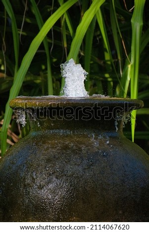 Moment shot of a giant vase that serves as a fountain. The photo was taken in the Maldives during a vacation, in the background you can see green tropical leaves.