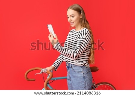 Pretty teenage girl with bicycle using mobile phone on red background