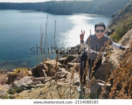 Beautiful brunette on the rocky shore of the lake. Woman in sportswear and black sunglasses.