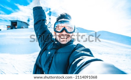 Young man taking selfie picture with smart cell phone hiking mountain on snowy slope - Happy skier having fun in ski resort vacation - Winter lifestyle, extreme sport and happy people concept