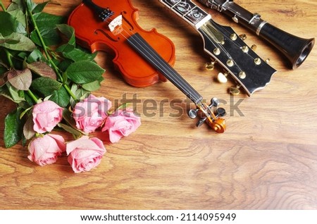 Violin, clarinet, electric guitar and a bouquet of roses on a wooden table.
