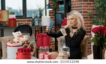 Elegant lovely beautiful girlfriend holding smartphone taking selfie with red roses enjoying romantic gift from boyfriend. Attractive blonde woman celebrating romance anniversary advertising event Royalty-Free Stock Photo #2114112248
