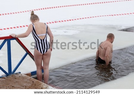 White young woman and old man bathes in icy water in an ice hole. Outdoor winter sports.