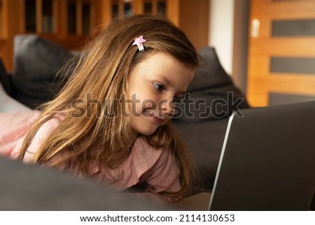 Cheerful little girl using laptop. Beautiful girl watching cartoon on laptop.